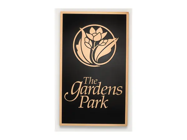 An example of a tall park sign plaque with a flower emblem and the words The Gardens Park