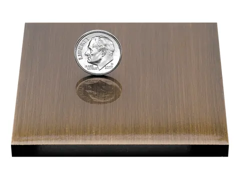 An oxidized bronze sample plate, darkened for an aged look, with a dime on it for scale